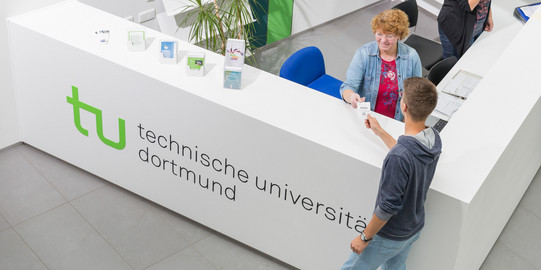 A person from the Academic Advice team is handing over a queue ticket to a student.